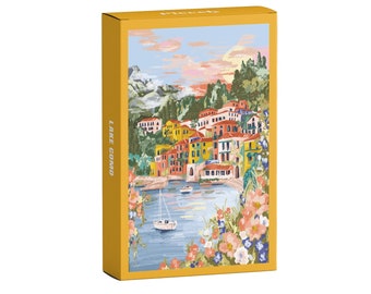 May include: A colorful illustration of a town on Lake Como, Italy. The image features a picturesque waterfront with colorful buildings, lush greenery, and a sailboat on the water. The text "LAKE COMO" is printed on the side of the box.
