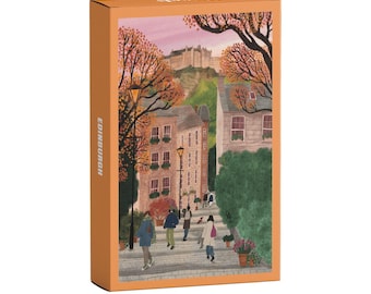 Könnte beinhalten: Eine rechteckige Schachtel mit orangefarbenem Rand und einer Illustration einer Straßenszene in Edinburgh. Das Bild zeigt Menschen, die auf einem Kopfsteinpflasterweg zwischen Steingebäuden, herbstlichen Bäumen und einer Burg auf einem Hügel gehen.