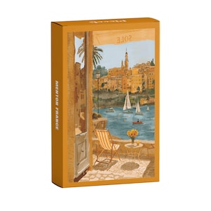 May include: A mustard-colored box featuring a watercolor painting of Menton, France. The artwork depicts a seaside scene with sailboats, buildings, and a cafe table with a striped chair. The text "MENTON FRANCE" is printed vertically on the side.