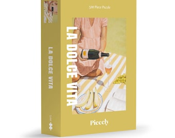 May include: A 500 piece jigsaw puzzle featuring a woman in a pink dress sitting on a striped blanket with a glass of wine and a bottle of champagne. The puzzle is titled "La Dolce Vita" and is made by Piecely.