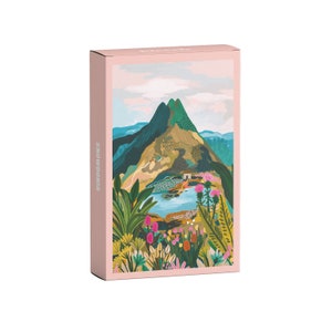 Könnte beinhalten: Eine rosa Box mit dem Wort "SNOWDONIA" auf der Seite. Die Box zeigt eine farbenfrohe Illustration einer Bergkette mit einem See und Wildblumen.