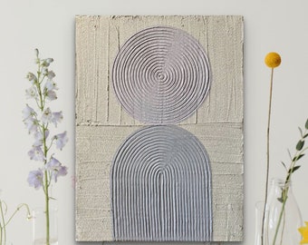 May include: Textured abstract art piece with a beige background and two geometric shapes in shades of gray. The top shape is a circle, and the bottom is an arch. The artwork is displayed against a white wall, with flowers in vases on either side.