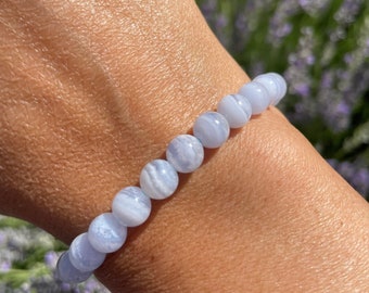 May include: A blue agate beaded bracelet with a light blue and white banded pattern. The bracelet is worn on a person's wrist.