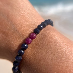 May include: A bracelet made of dark blue and pink gemstone beads. The bracelet is worn on a person's wrist.