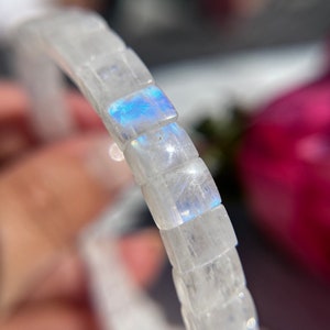 May include: A clear, square-beaded bracelet. The beads have an iridescent sheen, with flashes of blue and white light. The bracelet is strung together, creating a flexible piece of jewellery.