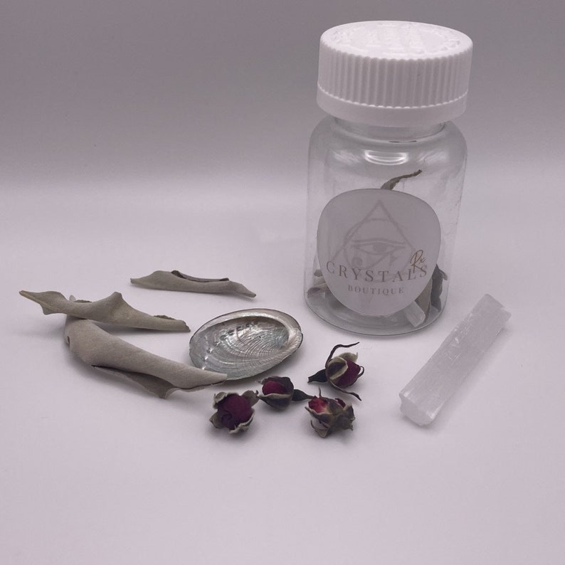 May include: A collection of spiritual items including a clear bottle with a white lid, a small abalone shell, dried rose buds, sage bundles, and a white selenite crystal wand. The bottle has a label that reads "Crystals Boutique".