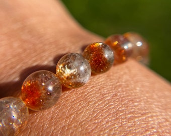 May include: A bracelet made of round, translucent, golden sunstone beads with a shimmery, iridescent finish.