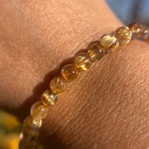 May include: A gold and clear beaded bracelet with a stretchy band. The beads are round and have a natural, organic look.