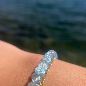 May include: A bracelet with clear, faceted beads and a gold chain. The bracelet is worn on a person's wrist.