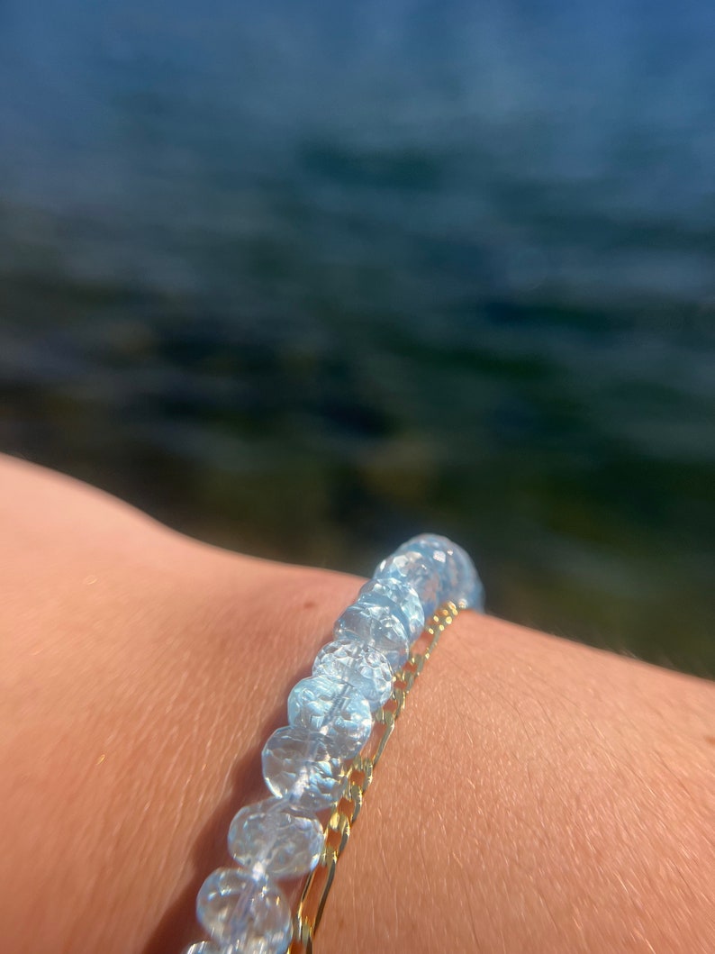 May include: A bracelet with clear, faceted beads and a gold chain. The bracelet is worn on a person's wrist.