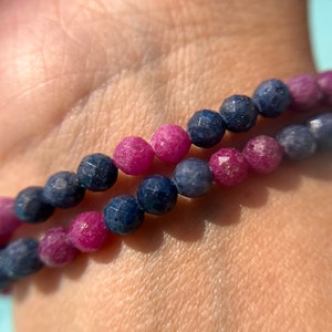 May include: A bracelet made of faceted blue and pink beads. The bracelet is worn on a person's wrist.