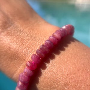 May include: A pink gemstone bracelet with faceted beads. The bracelet is worn on a person's wrist.