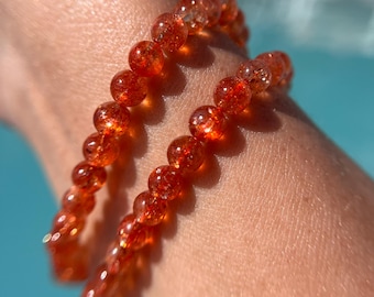 May include: Two bracelets made of orange sunstone beads. The beads are round and have a sparkly, iridescent finish.