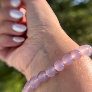 Puede incluir: Un brazalete hecho de cuentas de piedras preciosas de color púrpura claro. El brazalete se lleva en la muñeca.