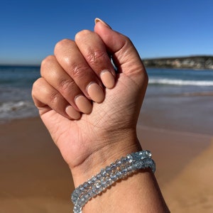 May include: A bracelet made of light blue aquamarine beads. The bracelet is worn on a person's wrist.