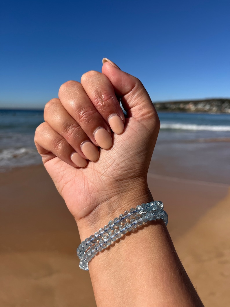 May include: A bracelet made of light blue aquamarine beads. The bracelet is worn on a person's wrist.