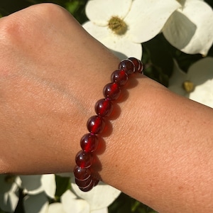 May include: A red gemstone bracelet with round beads. The bracelet is worn on a person's wrist.