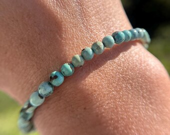 May include: A turquoise beaded bracelet with a simple design. The bracelet is made of small, round beads that are strung together on a clear elastic cord.