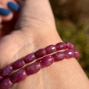 May include: A close-up of a pink gemstone bracelet with oval-shaped beads. The bracelet is made of natural stones and is worn on a person's wrist.