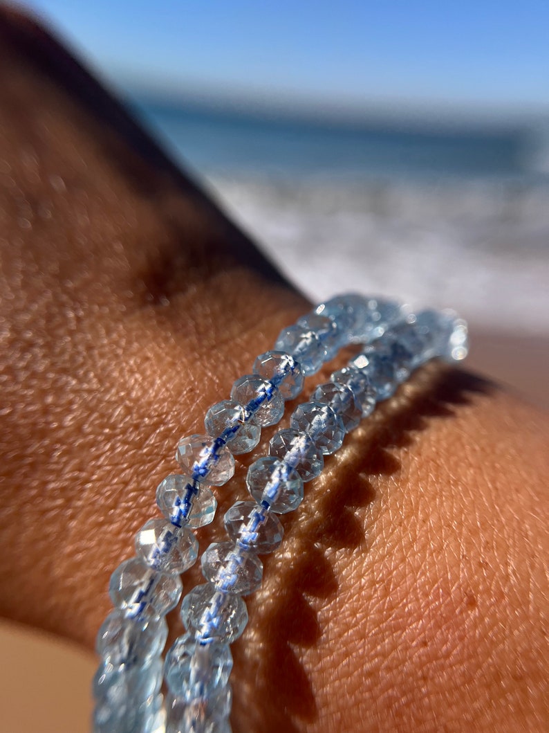 May include: A bracelet made of light blue faceted beads with a white and blue thread running through the beads.