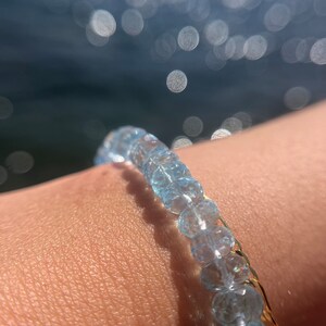 May include: A delicate bracelet made of light blue aquamarine beads with a gold chain accent.