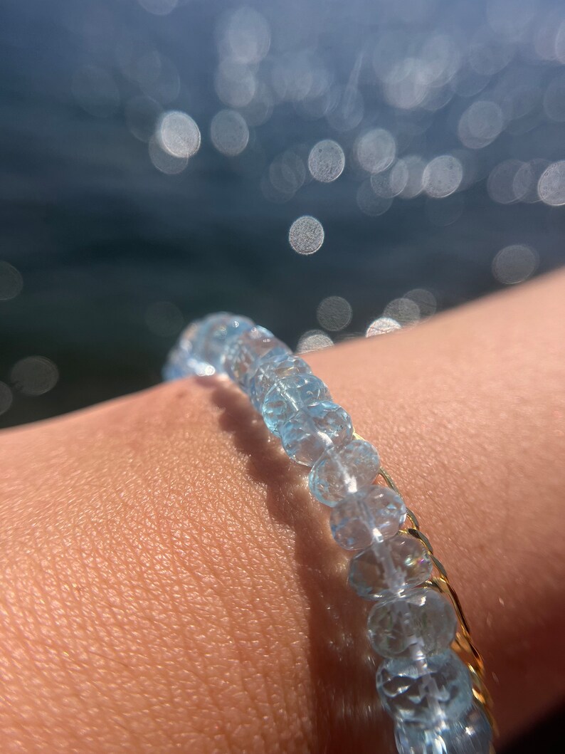 May include: A delicate bracelet made of light blue aquamarine beads with a gold chain accent.