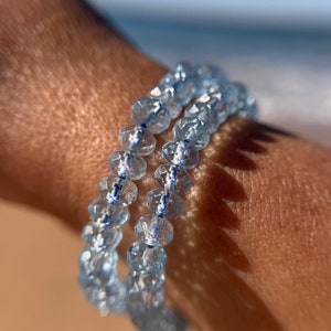 May include: A double-strand bracelet made of light blue faceted beads with a thin blue and white stripe running through the center of each bead.