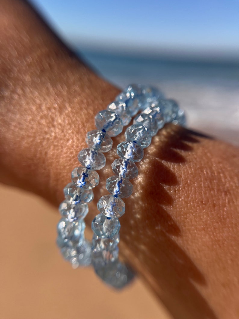 May include: A double-strand bracelet made of light blue faceted beads with a thin blue and white stripe running through the center of each bead.