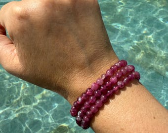 May include: A stack of three bracelets made with pink and white gemstone beads. The bracelets are worn on a person's wrist.