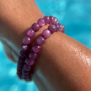 May include: A purple gemstone bracelet with iridescent beads. The bracelet is worn on a person's wrist.