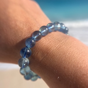 May include: A blue gemstone bracelet with round beads. The bracelet is on a person's wrist.