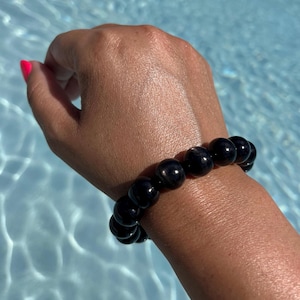 Peut inclure: Un bracelet noir composé de perles rondes et lisses. Le bracelet est porté au poignet.