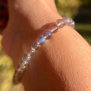 May include: A bracelet made of iridescent, light blue gemstone beads. The beads are round and smooth, and the bracelet is strung on a clear elastic cord.
