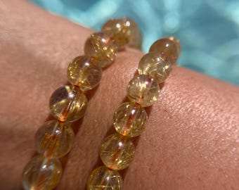 May include: A gold and clear crystal bracelet with a double strand of beads. The beads are round and have a golden shimmer.