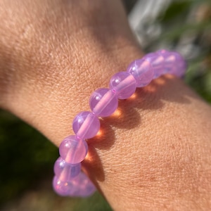May include: A bracelet made of light purple beads. The beads are round and have a slight shimmer to them.