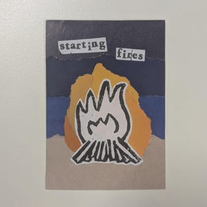 May include: A handmade collage with a bonfire illustration and the words "starting fires". The bonfire is white with black outlines, set against a yellow and orange background. The background has blue and tan paper layers.