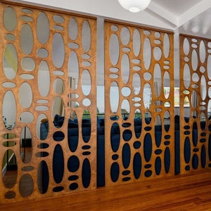 May include: A wooden room divider with a geometric pattern of oval cutouts. The divider is made of light brown wood and has a natural wood finish. The cutouts create a unique and modern design.