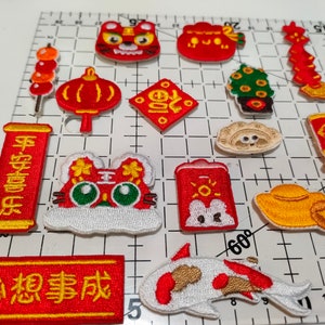 May include: A set of 13 embroidered iron-on patches featuring Chinese New Year symbols and characters. The patches are red, yellow, and white with gold accents. The patches include a tiger, a lantern, a koi fish, a lucky cat, and a red envelope.