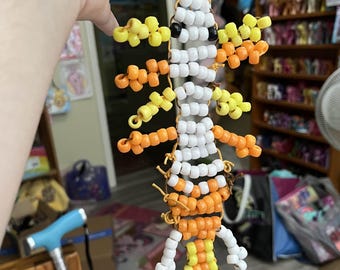 May include: A beaded lizard keychain in white, orange, and yellow. The lizard has a segmented body and limbs, with a black bead for an eye. The keychain is attached to a metal ring with orange string.