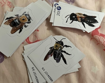 May include: A collection of white stickers featuring detailed illustrations of bumblebees. The bees are depicted with black and yellow bodies, brown wings, and intricate details. Some stickers have the numbers "201 P" printed on them.