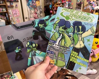 May include: Two comic book prints featuring cartoon characters with green and blue skin tones. One print shows a character in a futuristic setting, while the other displays the title "MEANT GREEN" with text and illustrations.