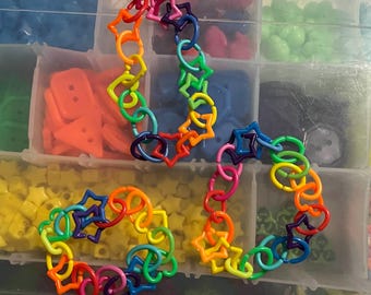 May include: A rainbow colored plastic chain necklace with star and heart shaped links. The necklace is made of multiple colors including red, orange, yellow, green, blue, indigo, and violet.