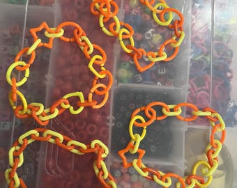May include: Four handmade bracelets in a plastic container. The bracelets are made of orange and yellow plastic chain links. Two bracelets have star-shaped links. The container is filled with beads of various colors.
