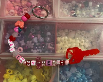 May include: A beaded bracelet with the words "TO MY HEART" spelled out in colorful letter beads. The bracelet features various shaped beads, including hearts, strawberries, and butterflies. A red key charm and a silver keyring are also present.