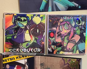 May include: Two square art prints featuring colorful cartoon characters with holographic accents. One print has the text "OCROBOTOR" and the other has the text "HD.1". The characters have green, purple, and pink skin tones.