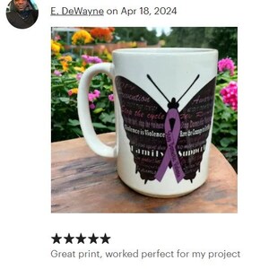 May include: White ceramic mug with a purple butterfly design. The butterfly has the words "Stop the cycle" and "Family Support" printed on its wings. The mug is on a wooden surface.