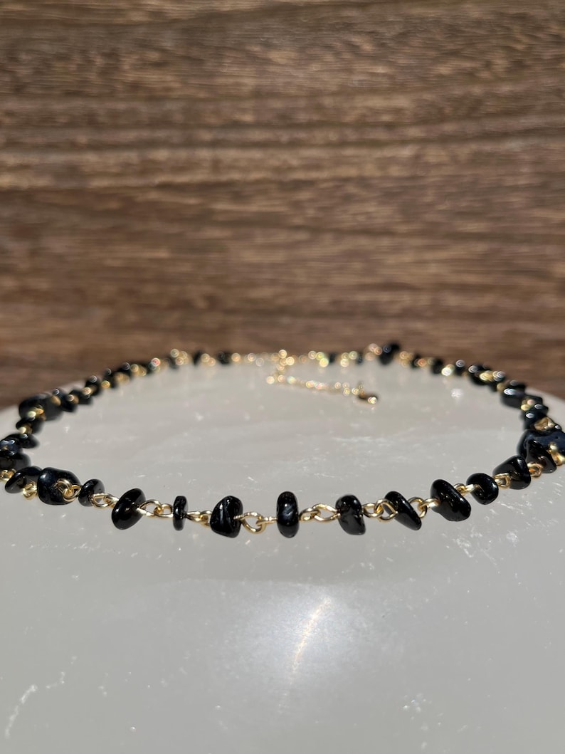 May include: A delicate black choker necklace with small, irregular black stones connected by a gold chain.
