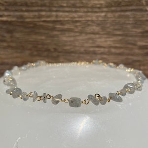 Puede incluir: Un delicado collar de cadena dorada con peque&ntilde;as piedras grises irregulares. Las piedras est&aacute;n conectadas por peque&ntilde;os eslabones dorados. El collar est&aacute; sobre una superficie blanca.