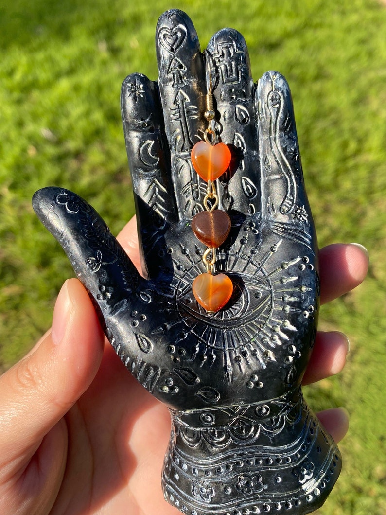 May include: Gold dangle earrings with three orange heart-shaped carnelian beads.