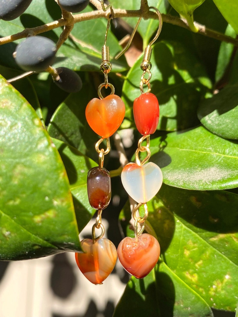 May include: Gold heart-shaped earrings with carnelian and agate beads. The earrings have a layered design with three beads on each earring.